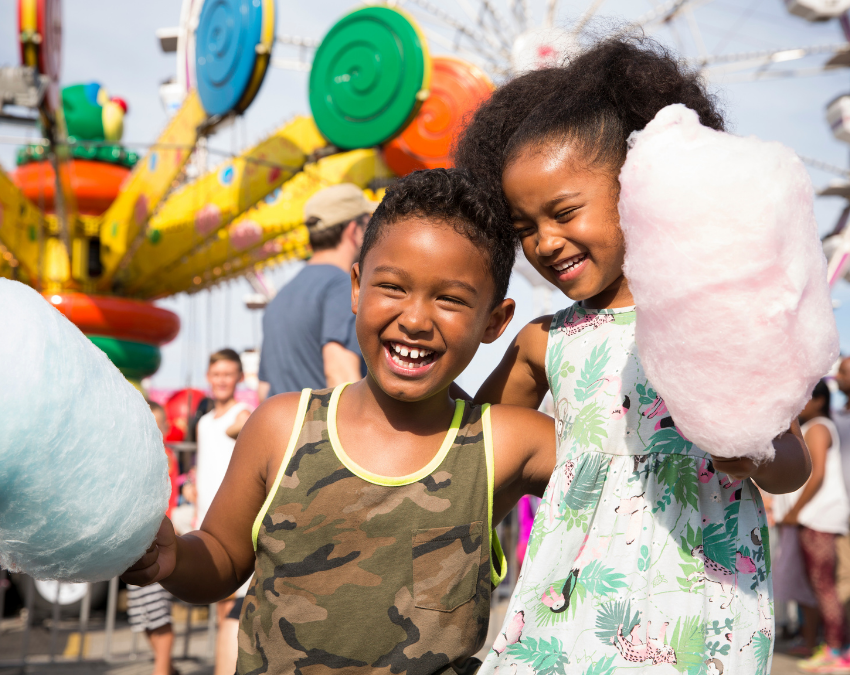 Two children smiling with cotton candy, a boy and a girl.