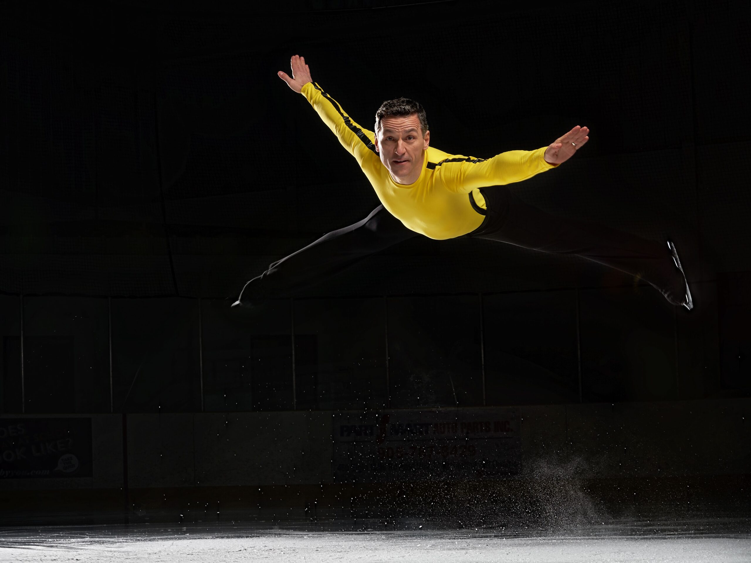 Elvis Stojko jumping high from the ice with arms spread, black background